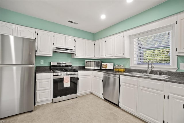 kitchen featuring under cabinet range hood, dark countertops, a sink, and appliances with stainless steel finishes