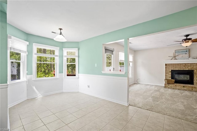 unfurnished living room with baseboards, a brick fireplace, ceiling fan, light tile patterned flooring, and light carpet