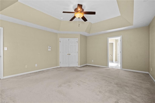 carpeted empty room featuring a tray ceiling, baseboards, and a ceiling fan