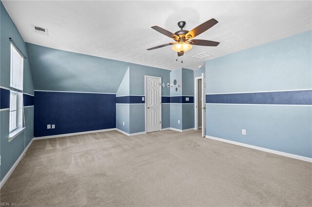 carpeted empty room with lofted ceiling, visible vents, baseboards, and ceiling fan