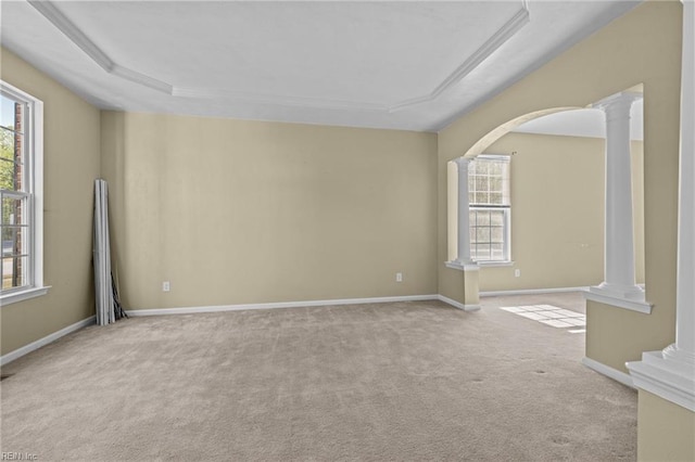 carpeted empty room featuring a tray ceiling, ornate columns, baseboards, and arched walkways