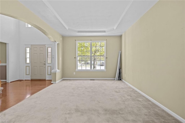 carpeted foyer entrance featuring a raised ceiling, arched walkways, crown molding, and baseboards
