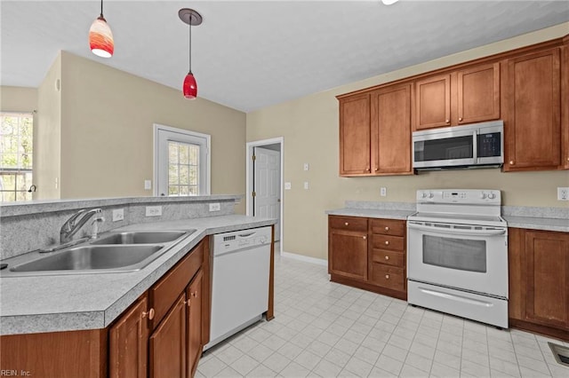 kitchen with white appliances, brown cabinetry, light countertops, a sink, and hanging light fixtures