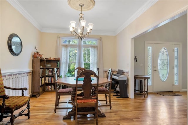 dining space with ornamental molding, an inviting chandelier, and light wood-style floors