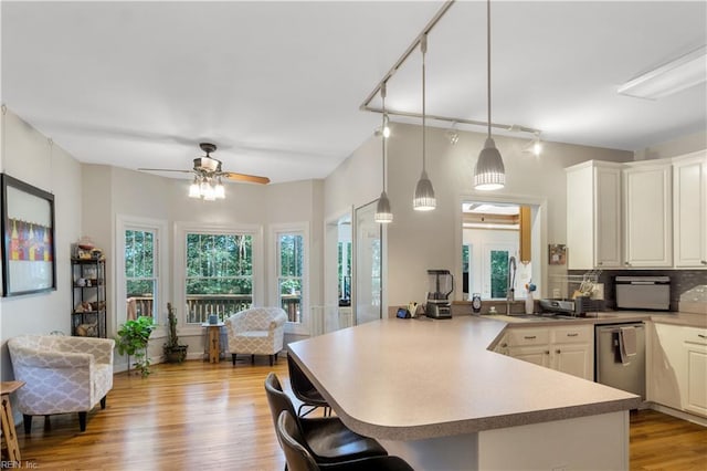 kitchen with a kitchen breakfast bar, a peninsula, backsplash, light wood-style floors, and stainless steel dishwasher
