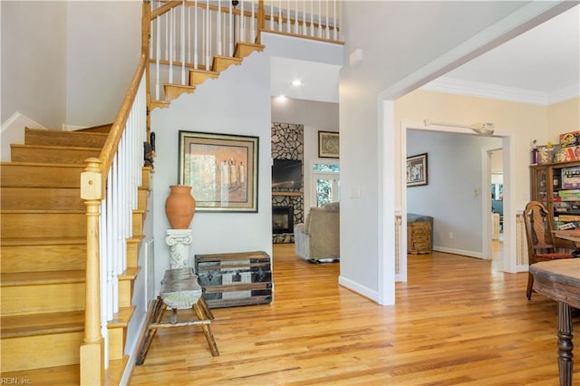 interior space featuring crown molding, a stone fireplace, a high ceiling, wood finished floors, and baseboards