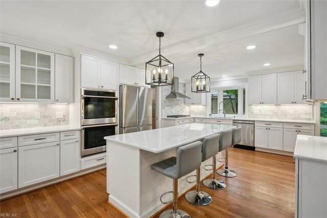 kitchen with tasteful backsplash, wall chimney range hood, white cabinetry, and stainless steel appliances