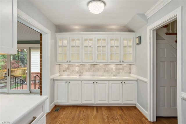 bar with light wood-type flooring, ornamental molding, backsplash, and visible vents
