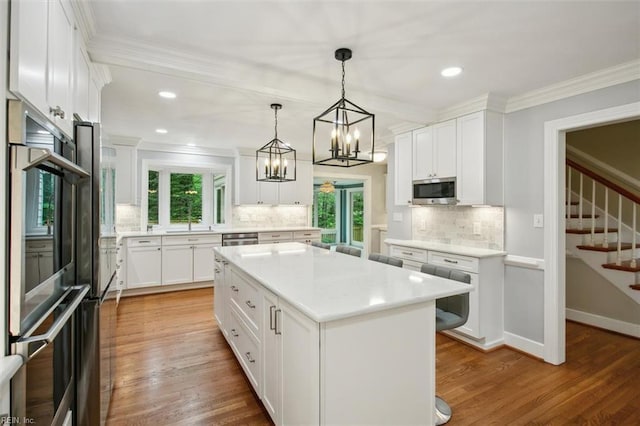 kitchen with crown molding, white cabinetry, appliances with stainless steel finishes, light countertops, and backsplash