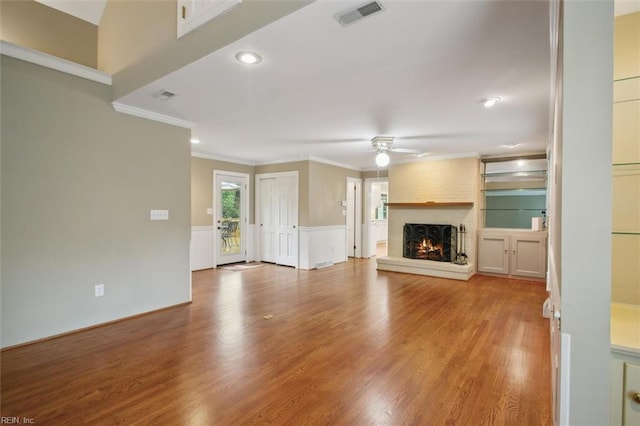 unfurnished living room featuring wood finished floors, a brick fireplace, a ceiling fan, and visible vents