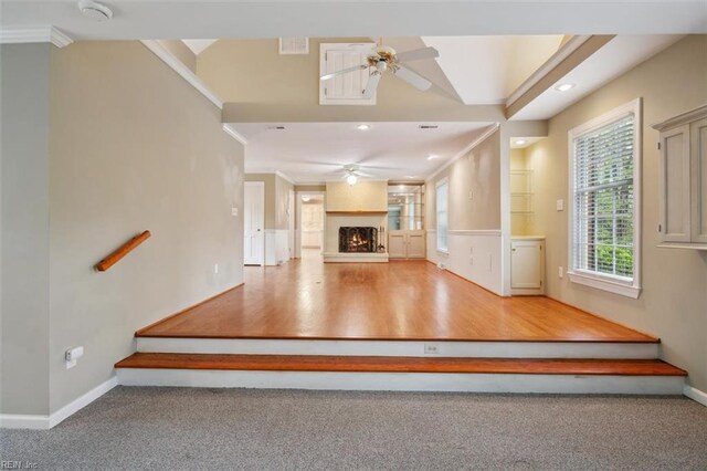 unfurnished living room featuring crown molding, ceiling fan, a lit fireplace, visible vents, and baseboards