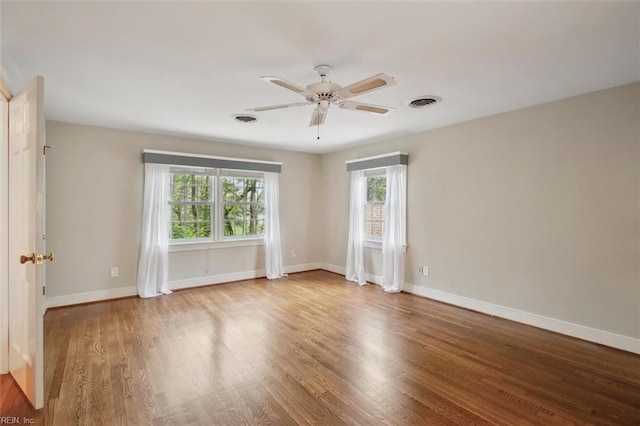spare room featuring wood finished floors, baseboards, a ceiling fan, and visible vents