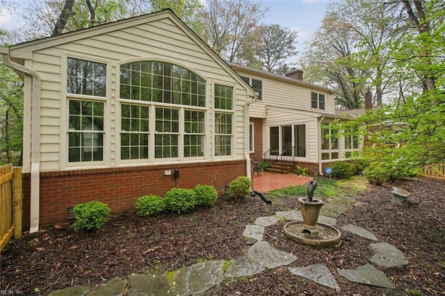 rear view of house featuring a sunroom, crawl space, fence, brick siding, and a chimney