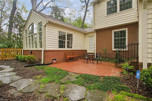 rear view of house with brick siding, entry steps, fence, and a patio area