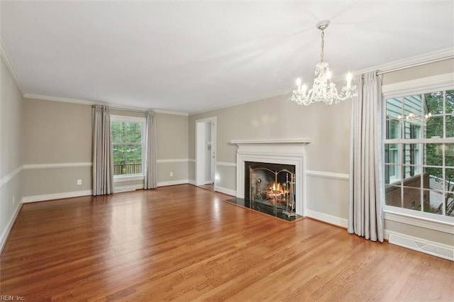unfurnished living room featuring baseboards, a lit fireplace, ornamental molding, a chandelier, and wood finished floors