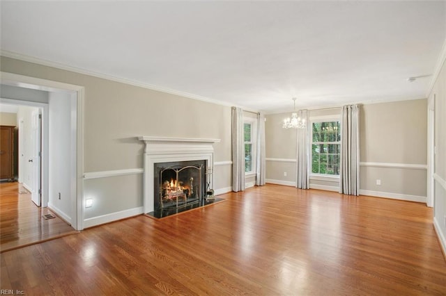 unfurnished living room with wood finished floors, a notable chandelier, ornamental molding, and a warm lit fireplace