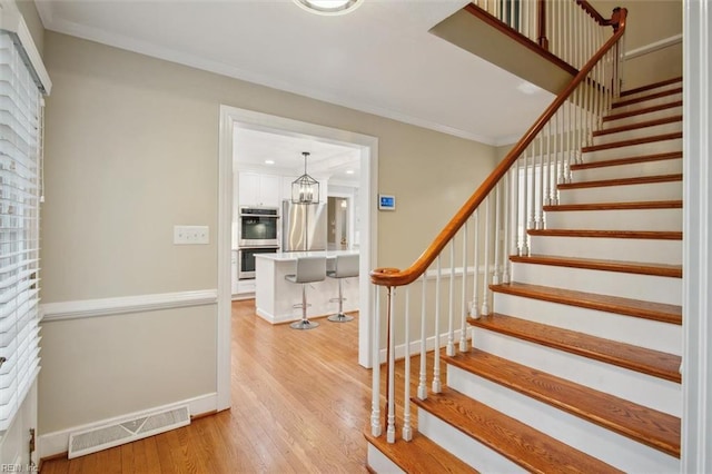 stairs featuring a notable chandelier, baseboards, crown molding, visible vents, and wood finished floors