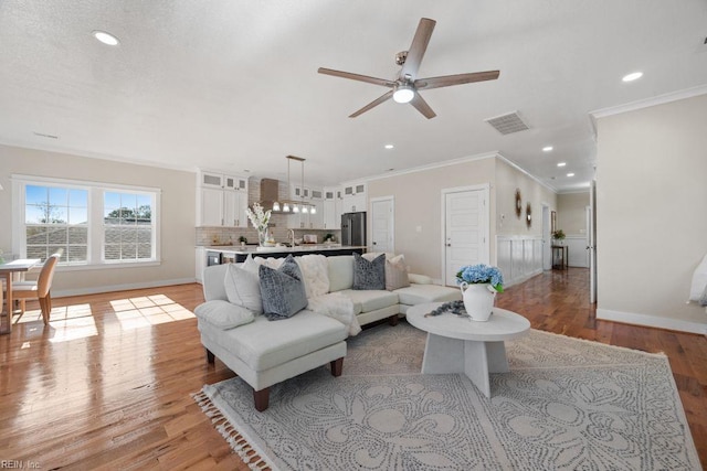 living area featuring visible vents, baseboards, a ceiling fan, crown molding, and light wood-style flooring