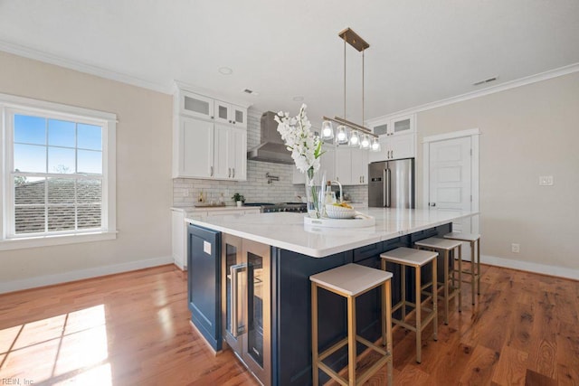 kitchen with high end refrigerator, crown molding, backsplash, and wall chimney range hood