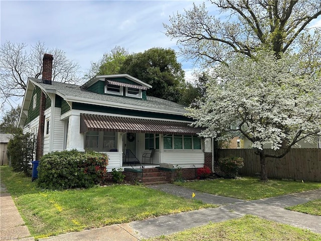 bungalow-style home featuring a shingled roof, a front lawn, fence, and a chimney