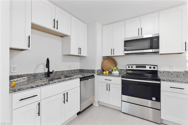 kitchen featuring dark stone countertops, appliances with stainless steel finishes, a sink, and white cabinetry