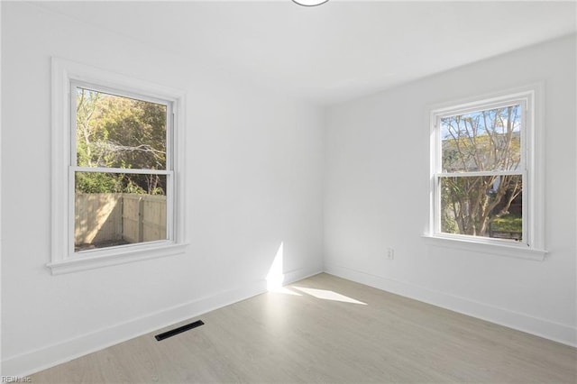 unfurnished room featuring plenty of natural light, visible vents, baseboards, and wood finished floors
