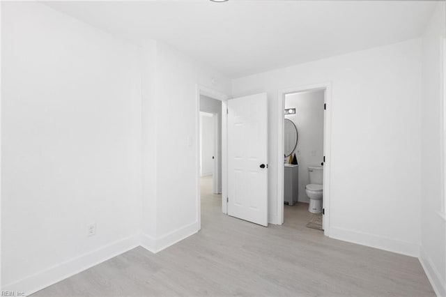 unfurnished bedroom with light wood-type flooring, baseboards, and connected bathroom