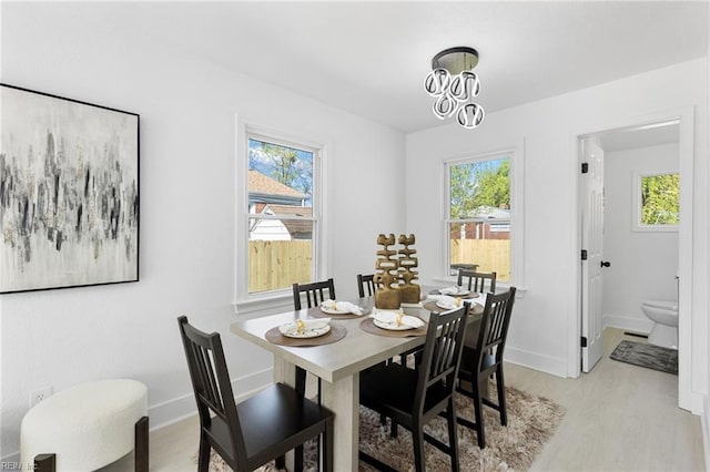 dining area featuring light wood-style flooring, a healthy amount of sunlight, an inviting chandelier, and baseboards