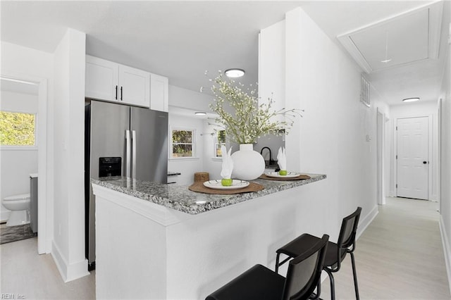 kitchen with stainless steel refrigerator with ice dispenser, light wood-style floors, white cabinetry, light stone countertops, and a breakfast bar area