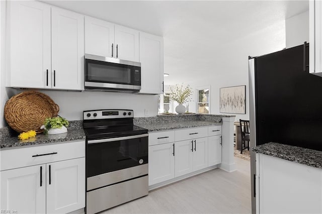 kitchen featuring dark stone counters, light wood-type flooring, appliances with stainless steel finishes, and white cabinets