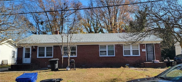 view of front facade featuring brick siding, roof with shingles, a front lawn, and a chimney
