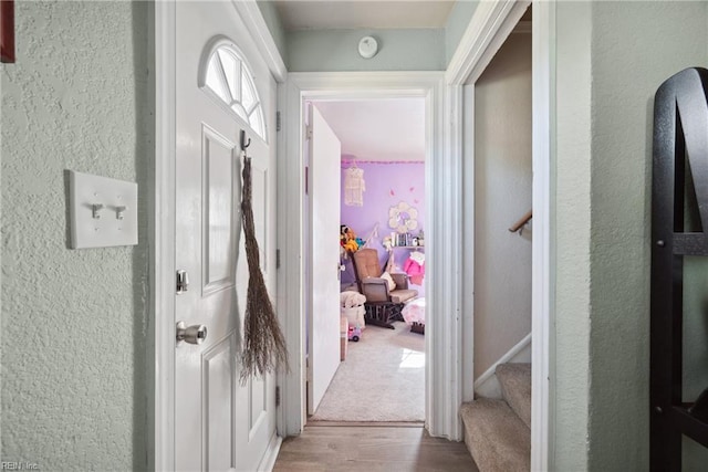hall featuring a textured wall, stairs, and wood finished floors
