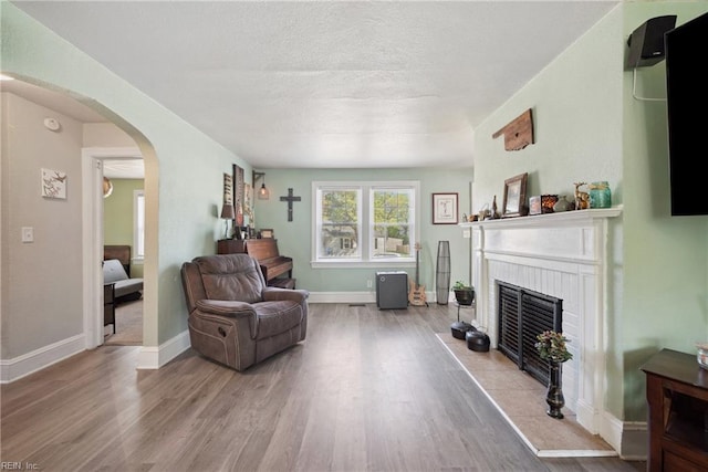 living room featuring baseboards, arched walkways, a brick fireplace, a textured ceiling, and light wood-style flooring