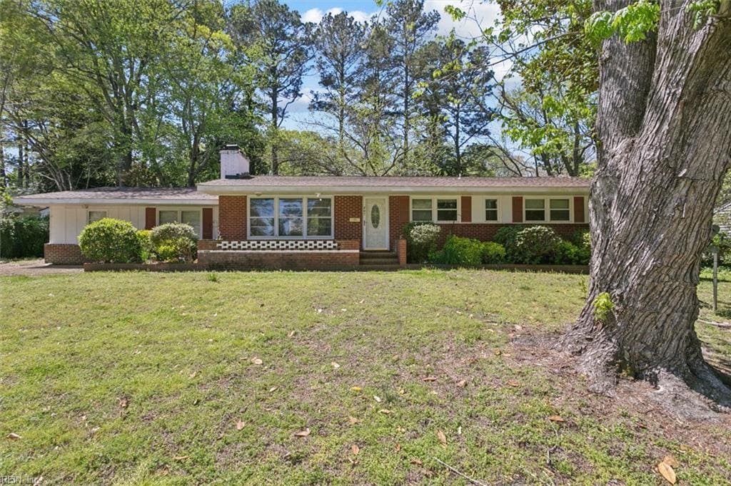 ranch-style house with brick siding, a chimney, and a front lawn