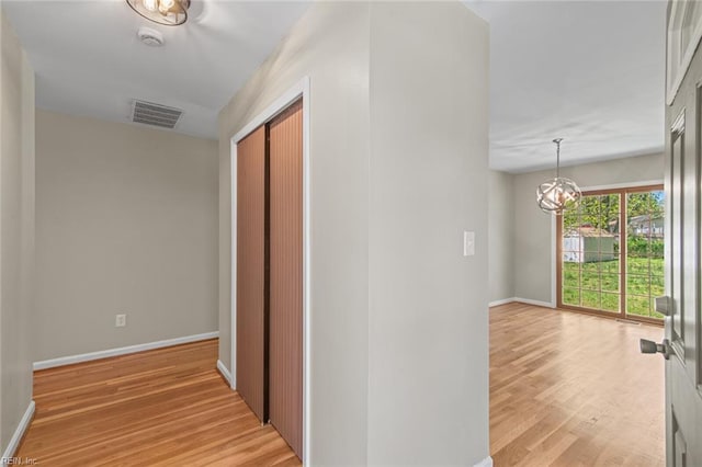 corridor featuring baseboards, light wood-style floors, a notable chandelier, and visible vents