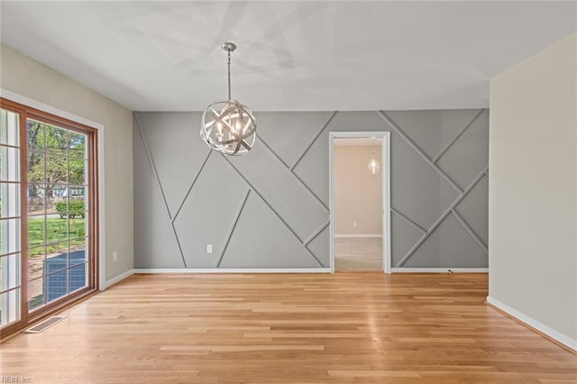 unfurnished dining area with a decorative wall, light wood finished floors, baseboards, and an inviting chandelier