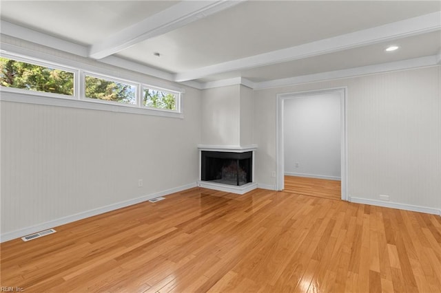 unfurnished living room featuring visible vents, a wealth of natural light, light wood-style floors, and beamed ceiling