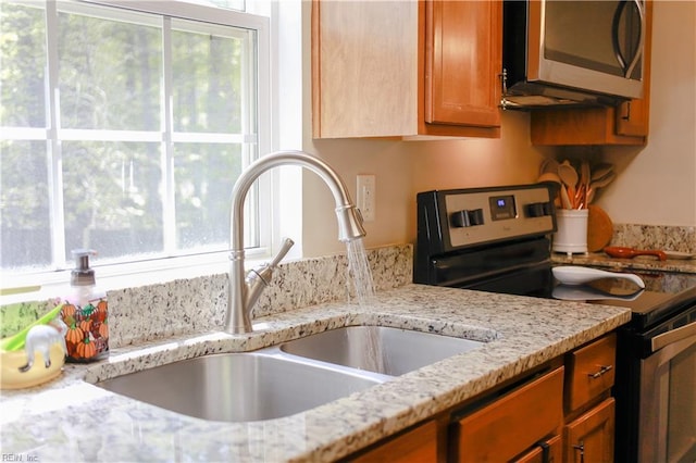 kitchen with brown cabinetry, light stone countertops, appliances with stainless steel finishes, and a sink