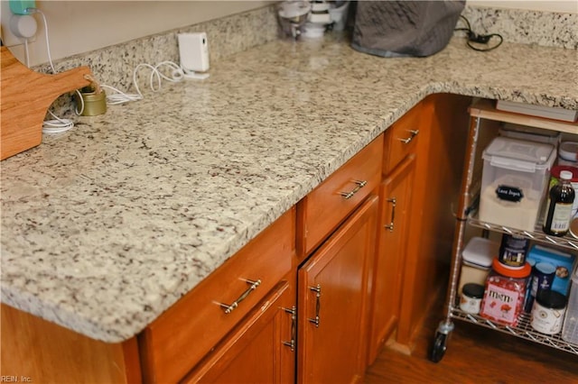 interior details featuring brown cabinetry, tasteful backsplash, light stone countertops, and dark wood-type flooring