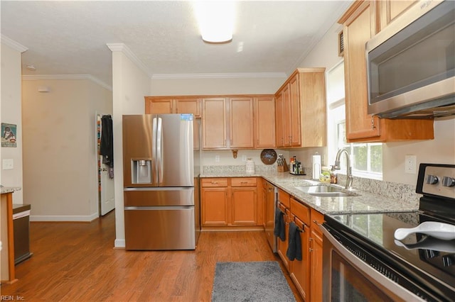 kitchen featuring light stone counters, a sink, light wood-type flooring, crown molding, and appliances with stainless steel finishes