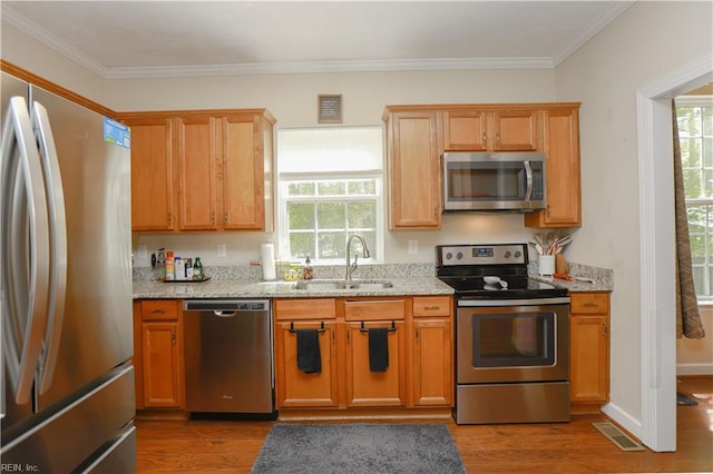 kitchen with light stone counters, wood finished floors, ornamental molding, a sink, and appliances with stainless steel finishes