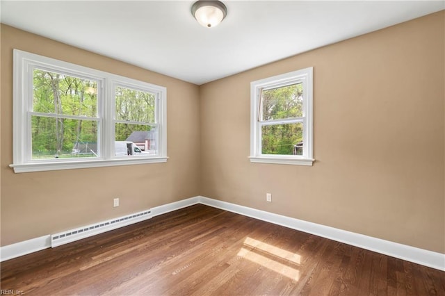 spare room featuring baseboards, plenty of natural light, a baseboard heating unit, and wood finished floors