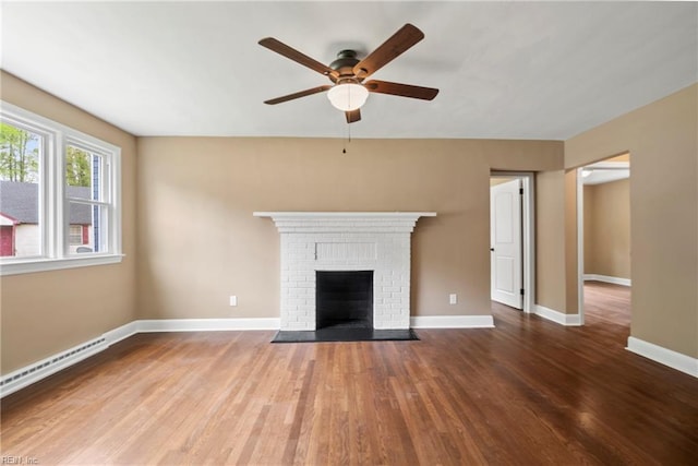 unfurnished living room with baseboards, a baseboard heating unit, a fireplace, ceiling fan, and wood finished floors