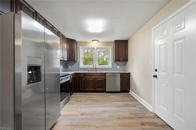 kitchen with dark brown cabinetry, light wood-style flooring, tasteful backsplash, appliances with stainless steel finishes, and a sink