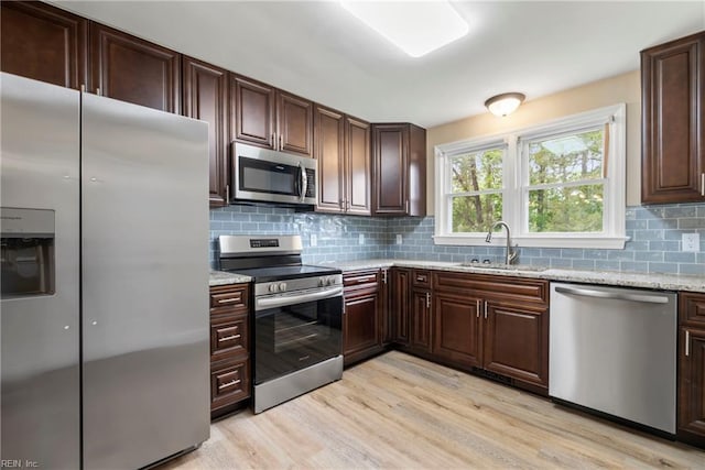 kitchen featuring light wood-style floors, light stone counters, a sink, stainless steel appliances, and decorative backsplash