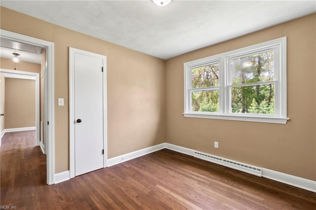 unfurnished bedroom featuring a baseboard radiator, attic access, baseboards, and dark wood-style floors