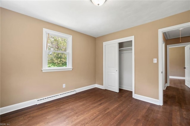 unfurnished bedroom featuring a closet, baseboard heating, wood finished floors, attic access, and baseboards