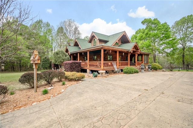 log cabin featuring log exterior, covered porch, and concrete driveway