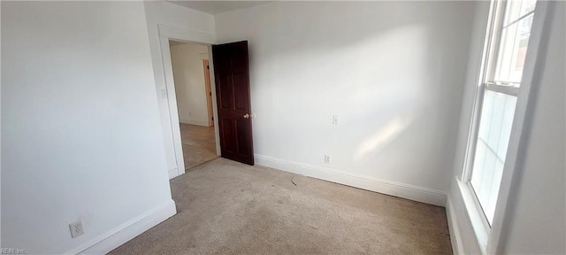 spare room with a wealth of natural light, light colored carpet, and baseboards