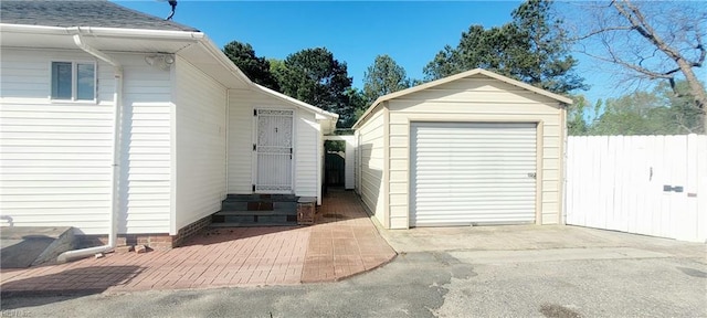 detached garage with fence, driveway, and a storage unit